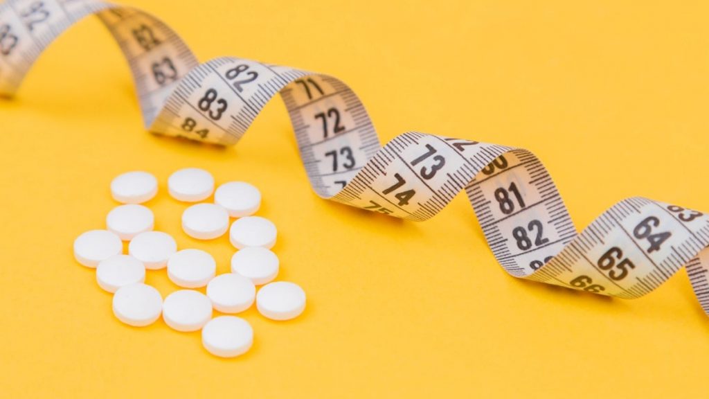 White measuring tape with a white pills, white vitamin on a yellow background. Diet. Slimming. Obesity. Place for an inscription. Weight loss marathon. Advertising. Top view. The close plan.